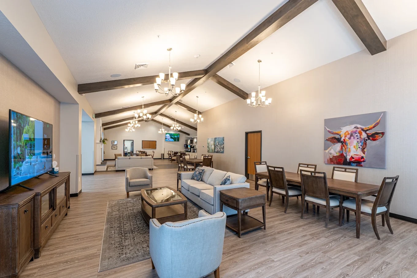 The great room, with vaulted wood-beam ceilings, chandeliers, sofas, and dining tables